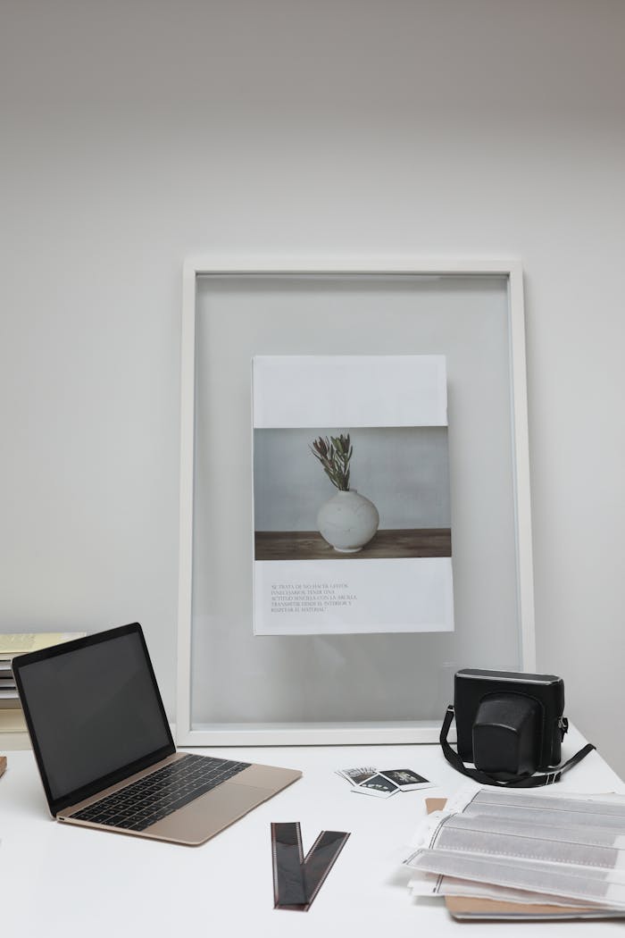 A neatly arranged workspace showing a laptop, camera, and framed art, ideal for creative professionals.